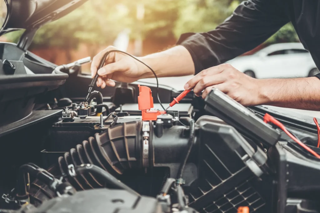 A mechanic uses a multimeter's red and black probes to test a car battery under an open hood.