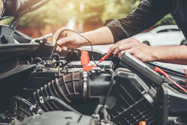 A mechanic uses a multimeter's red and black probes to test a car battery under an open hood.