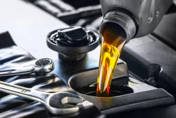 Amber motor oil pouring from a bottle into a car engine's oil fill opening beside two chrome wrenches.