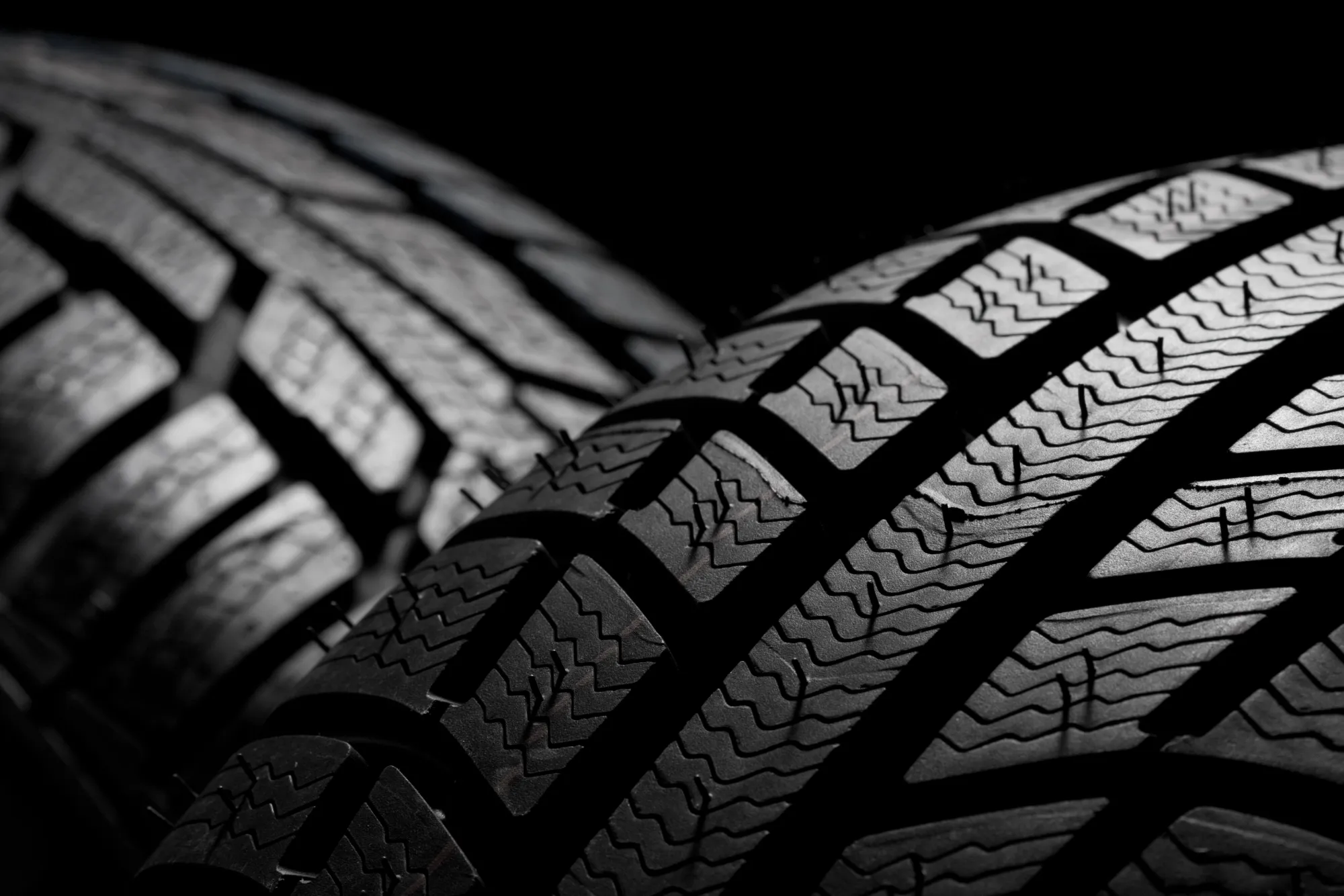 Extreme close-up of the grooved tread pattern on a new black tire against a dark background.